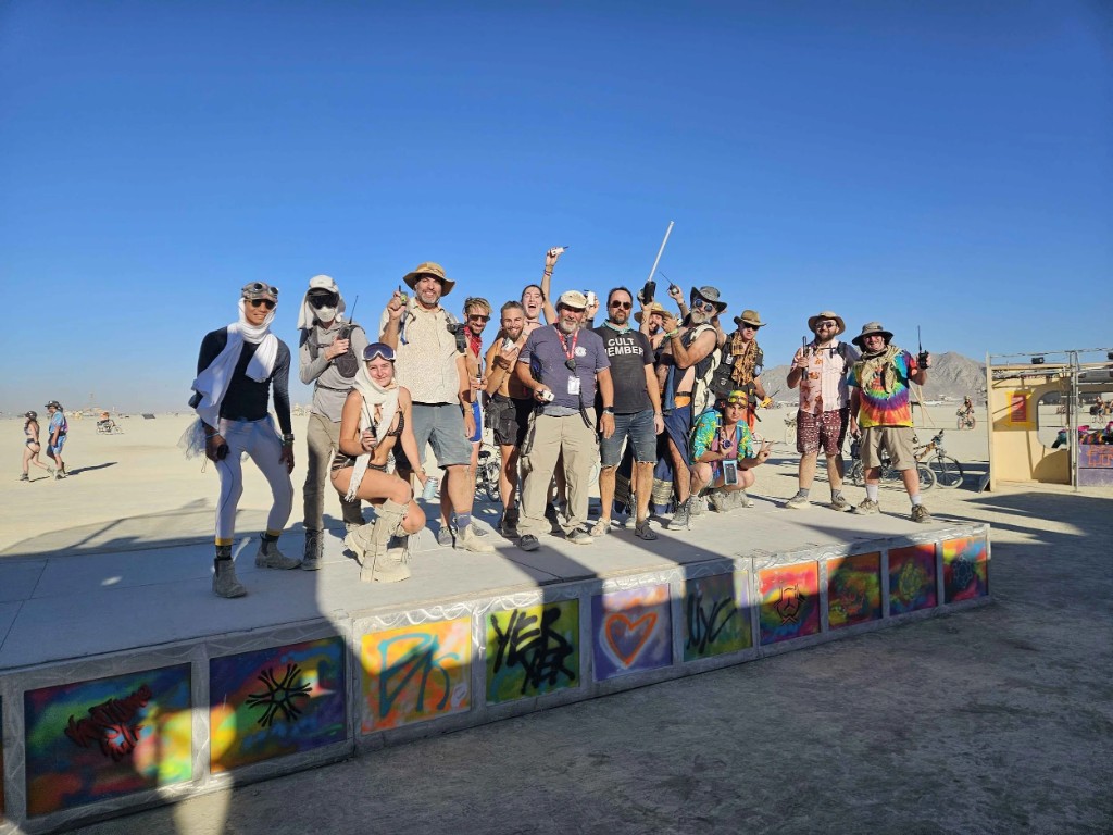 Burning Mesh volunteers posing on a playa stage, many holding radios