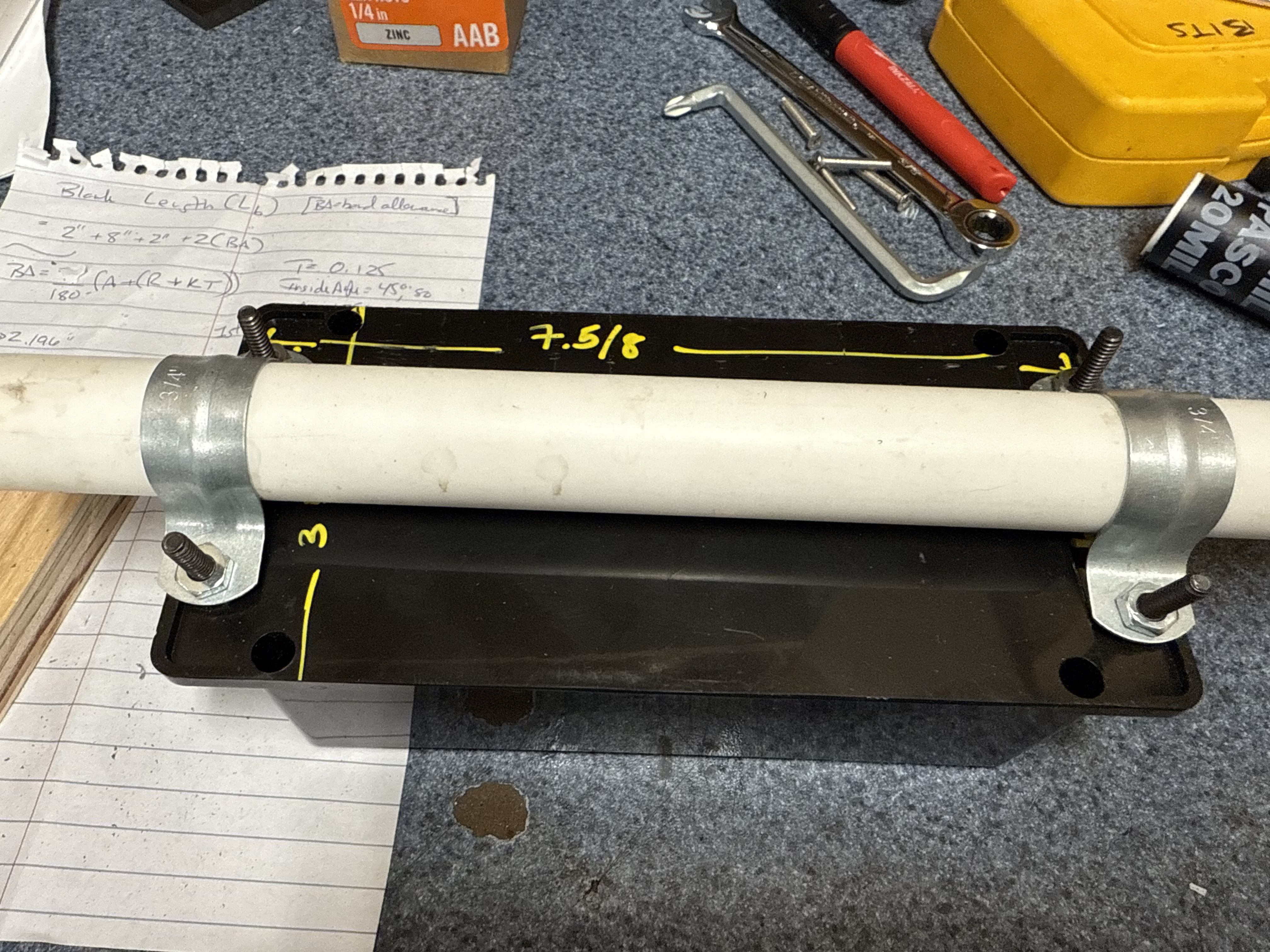Black enclosure with PVC pipe mount, conduit clamps, and handwritten bend-allowance notes on the bench