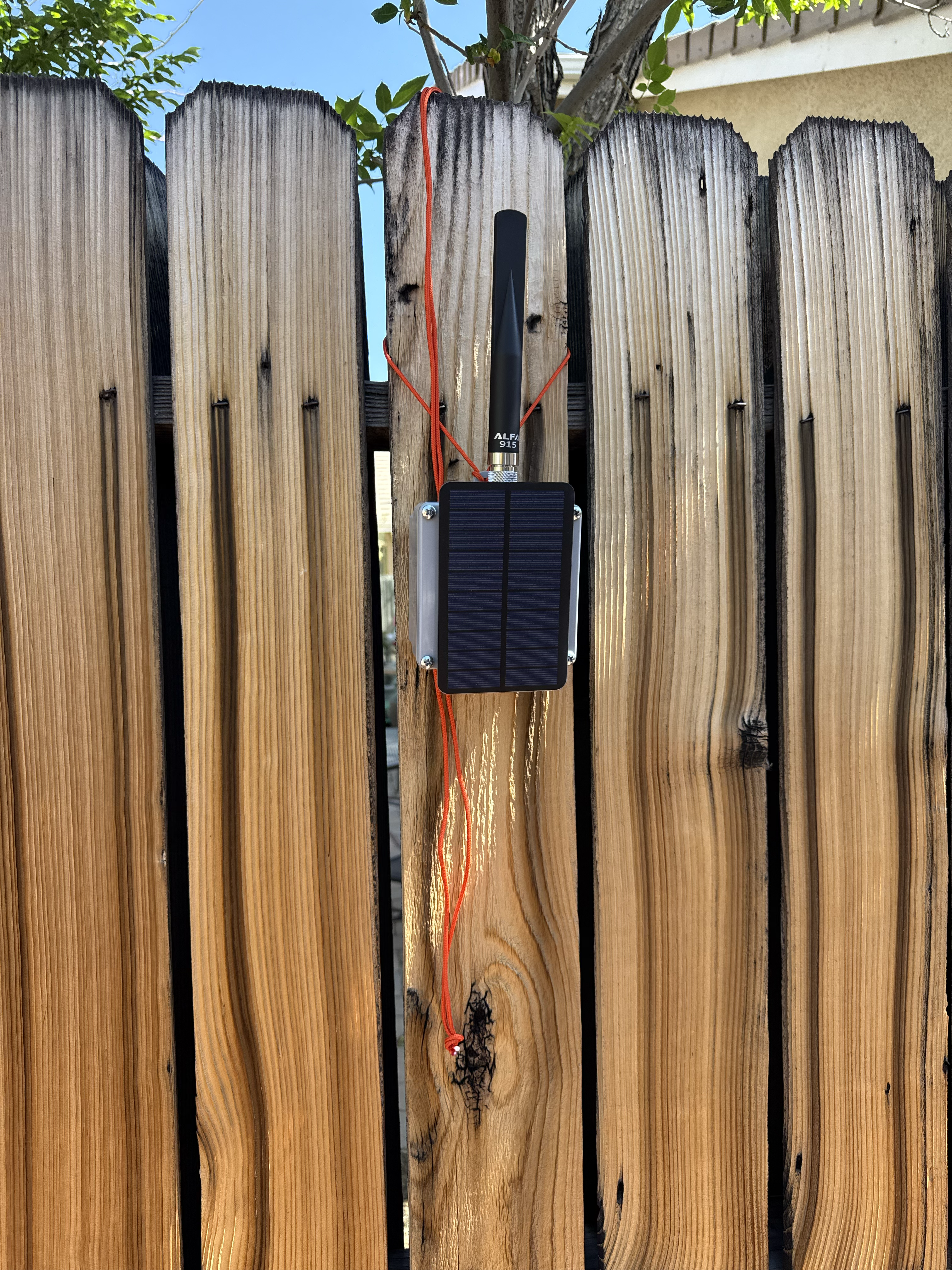 Compact solar-topped node with ALFA 915 antenna, paracord-mounted on a fence for field testing