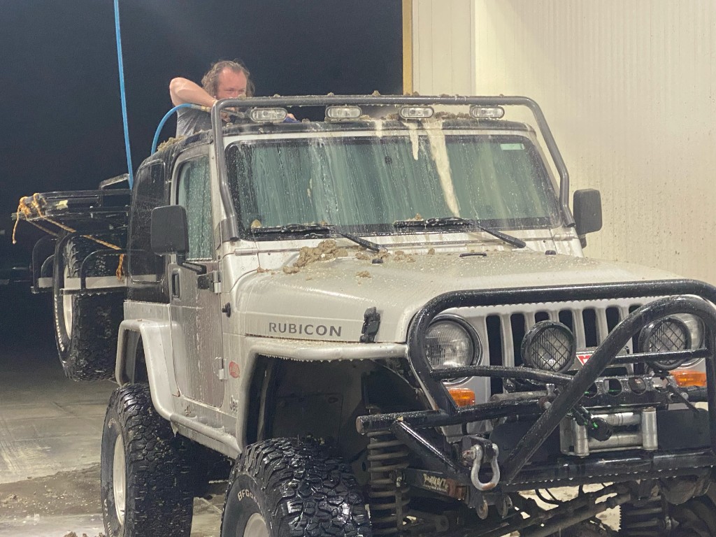 Jeep at a self-service car wash, mud clinging to the hood and roof rack