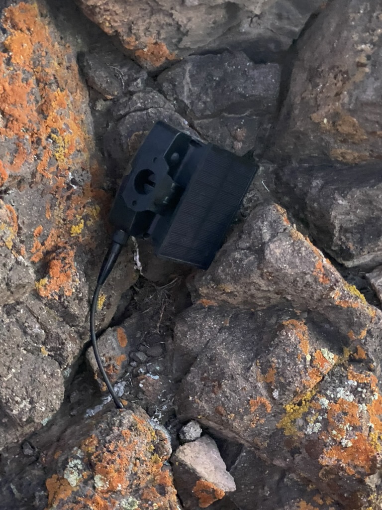 Ruslito wedged upside down between summit rocks, solar panel visible