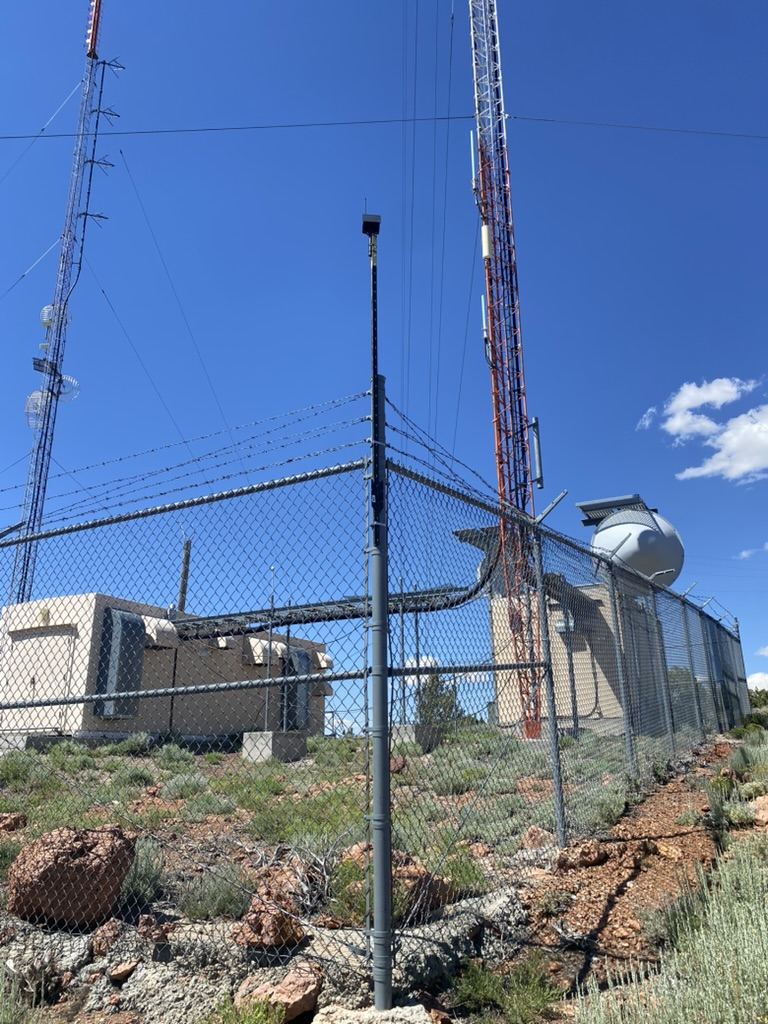 Mesh repeater staged on a fence post with communication towers in the background